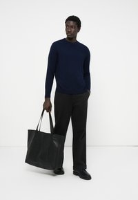 Navy knit sweater, black wide-leg trousers, and black leather tote bag. Smooth texture, simple design, and sturdy straps. Black shoes with grip.