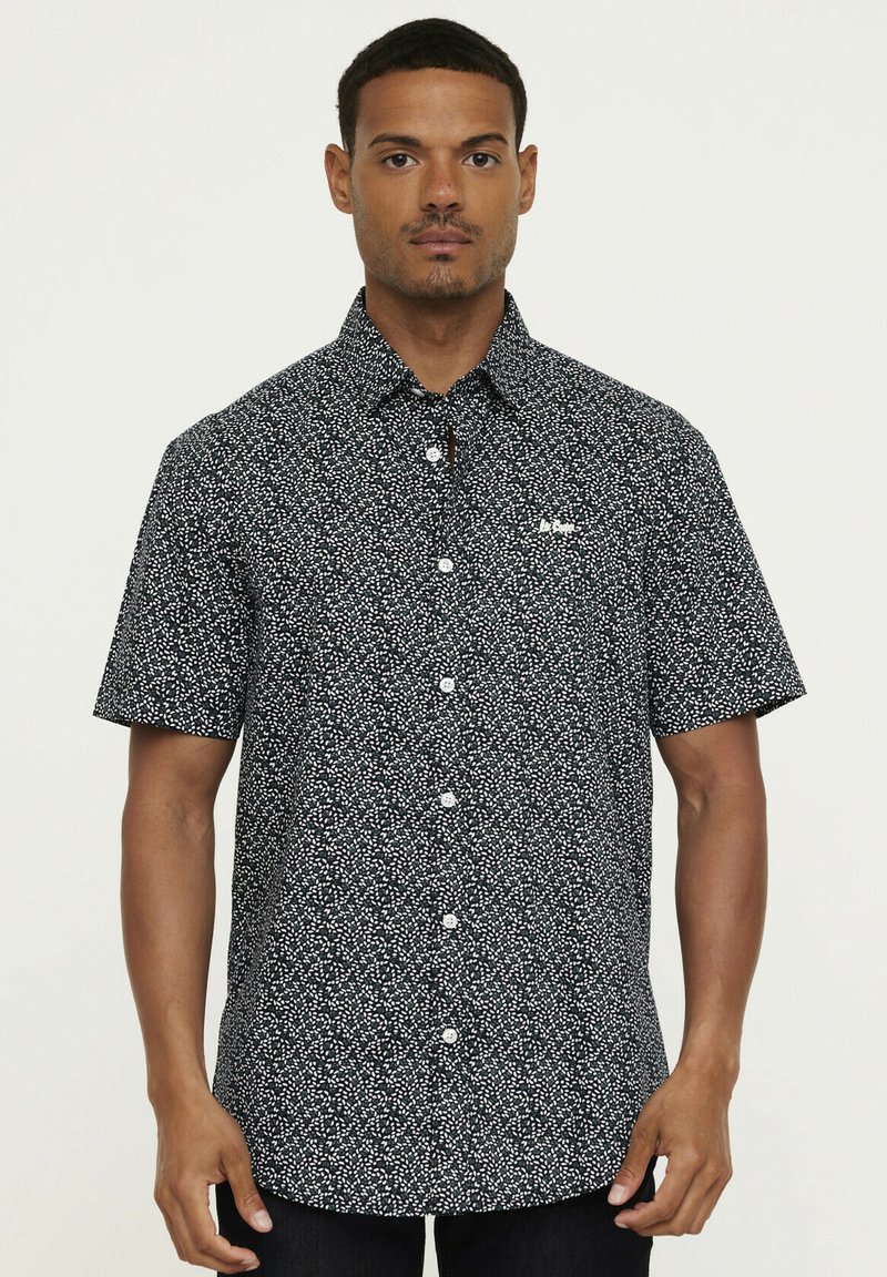 Chemise à manches courtes boutonnée en bleu marine foncé avec un motif à pois blancs, dotée d'un col classique et de boutons à l'avant.
