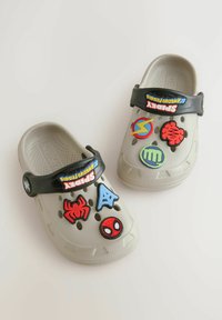 Helle graue Clogs mit schwarzem Riemen, die verschiedene bunte Gummi-Charms, einschließlich Spider-Man, Symbole und Logos auf der oberen Fläche zeigen.