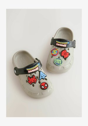Lys grå træskos med sort rem har forskellige farverige gummikarameller, herunder Spider-Man, symboler og logoer på den øverste overflade.