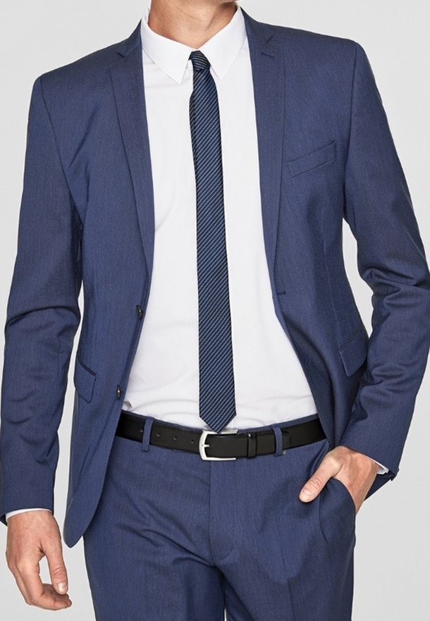 Marinblå kostym med slim fit, enfärgad kavaj. Vit skjorta och mönstrad slips. Svart läderbälte, slät tygtextur.