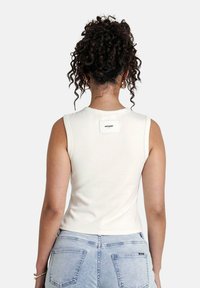 Top corto bianco senza maniche con scollatura rotonda; presenta un piccolo logo rettangolare sul retro; tessuto dalla superficie liscia.