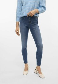 Jeans bleus taille haute avec une coupe slim, présentant un léger délavage et un design classique à cinq poches. Associés à un pull en tricot bleu clair.