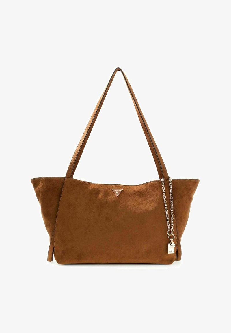 Sac bandoulière en daim marron avec longues bandoulières, un petit logo triangulaire Guess et une chaîne argentée avec deux breloques estampillées Guess.
