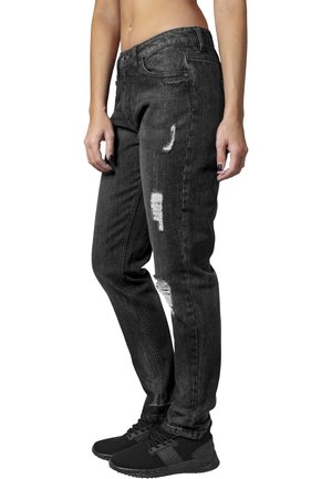 Svarte denimbukser med løs passform, med slitte detaljer og middels høy midje. Brukt med svarte treningssko.