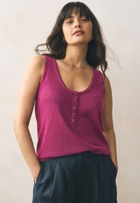 Canotta fucsia con scollo a V profondo, caratterizzata da un listino con cinque bottoni in tono oro. Tessuto morbido, vestibilità comoda, abbinata a pantaloni scuri.