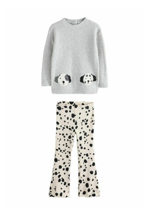 Pull en tricot gris avec des visages de chien sur les poches, associé à un pantalon crème avec des taches noires et des ourlets évasés.