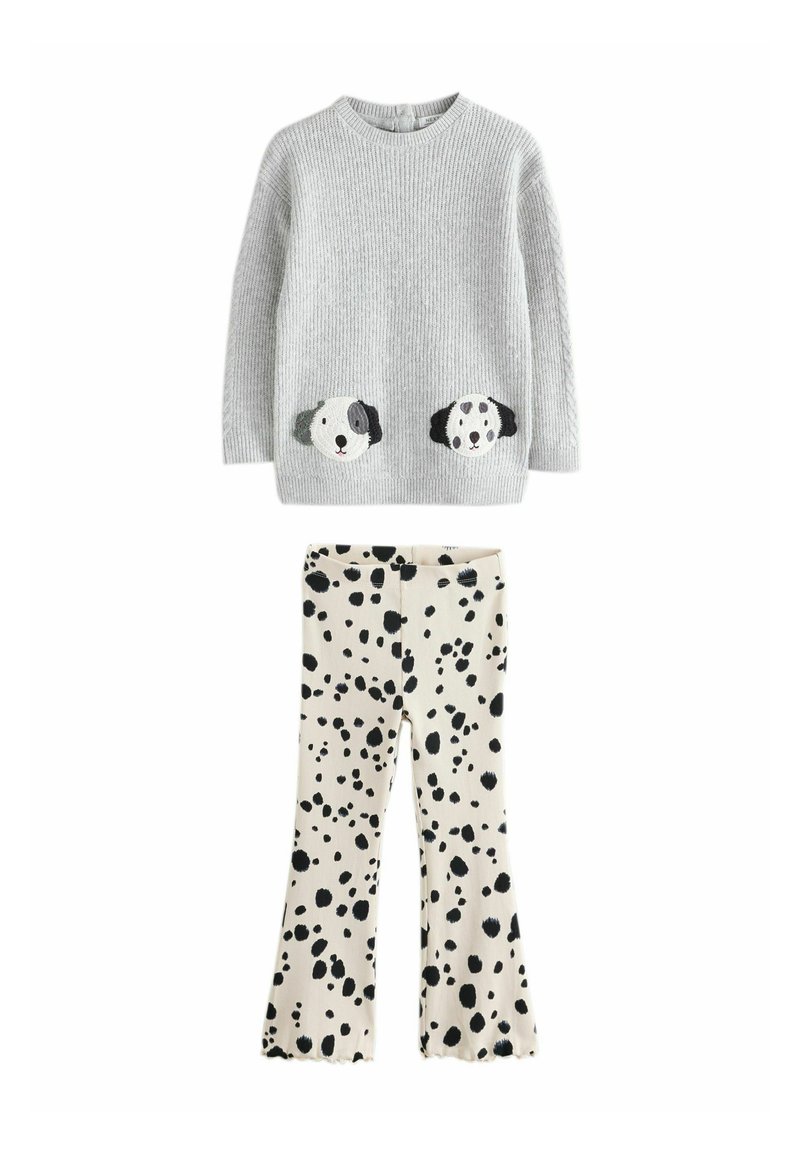 Maglione grigio lavorato a maglia con facce di cane sulle tasche, abbinato a pantaloni crema con macchie nere e orli svasati.