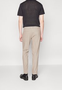 Beige broek gemaakt van een gladde stof, met een getailleerde pasvorm. Achterzijde bevat twee zakken en een discrete ritsdetail. Gekozen in combinatie met een zwart shirt.