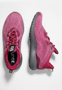 Baskets de sport roses avec dessus en maille respirante, motif texturé, bout rond et semelle en caoutchouc gris foncé. Présente des lacets et un talon renforcé.