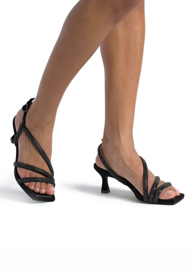Sandalias negras de tacón alto con múltiples correas cruzadas, un acabado texturizado y punta cuadrada. El tacón es corto y de tipo bloque.