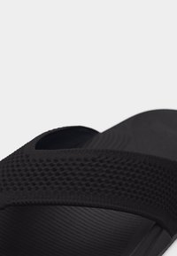 Közeli kép egy fekete, texturált papucsról, vastag pánttal és formázott talpbetéttel.