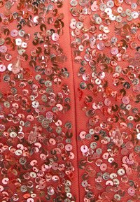 Tessuto corallo rivestito da una fitta disposizione di paillettes rotonde e lucide in diverse sfumature di rosa, con alcune gemme trasparenti.