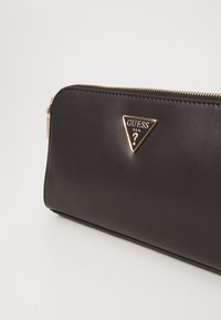 Černá kožená peněženka se zlatým trojúhelníkovým logem, zipovým uzávěrem a elegantním designem. Disponuje hladkým povrchem a kovovými akcenty.