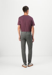 Pantalones grises con un corte ajustado y dos bolsillos traseros, combinados con una camiseta de manga corta color burdeos. Llevados con zapatillas casuales.
