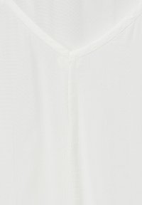 Vit blus med V-ringning och texturerad tyg. Den släta ytan och subtila glansen ger ett lätt utseende.