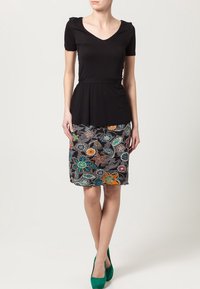 Haut noir à manches courtes avec un col en V et une taille cintrée, associé à une jupe crayon à motif floral. Le design présente des couleurs vives et des textures variées.