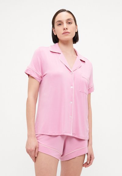 Pijamas cor-de-rosa com uma parte superior de botões de mangas curtas e um bolso no peito, acompanhados de calções combinando com piping branco contrastante. Material suave.