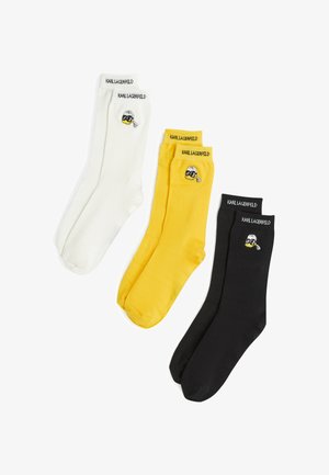Tres pares de calcetines: blancos, amarillos y negros. Cada uno presenta un logo con un personaje que lleva gafas de sol. Mezcla de algodón, textura suave.