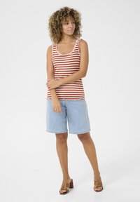 Top a righe rosso e crema, con bordi scallop; abbinato a pantaloncini di jeans blu chiaro. Sandali con tacco marroni.