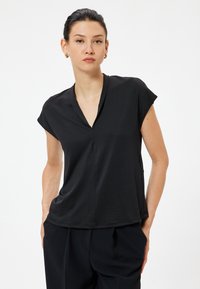 Sort kortærmet top med V-hals, lavet af blødt stof. Har en afslappet pasform og minimalistisk design, parret med høj taljebukser.