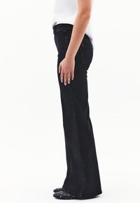 Mustat farkut, joissa on leveä lahje ja keski- korkea vyötärö, takataskussa erottuva punainen logo ja sileä pinta.