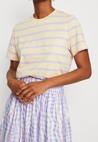 Striped t-shirt in light yellow and lavender, short sleeves, round neckline, paired with a pleated purple and lavender checkered skirt.