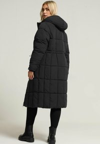 Czarna pikowana kurtka puchowa z kapturem, o długim kroju, z elastycznymi detalami na mankietach oraz gładką fakturą.