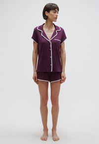 Lila rövid ujjú pizsamakészlet fehér szegéllyel, gombos inggel és hozzáillő rövidnadrággal, puha anyagból készült.