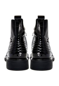 Paire de bottines en cuir noir brillant avec semelles épaisses et languettes, vues de dos sur un fond blanc.