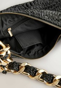 Schwarze geflochtene Handtasche mit einem goldenen Kettenriemen, ausgestattet mit einem Reißverschluss und schwarzem Stofffutter, das eine Innentasche zur Organisation bietet.