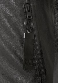 Schwarze Lederjacke mit Reißverschluss, die eine strukturierte Oberfläche und ein Lederetikett am Reißverschlusszug hat.