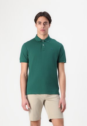 Mørkegrønn polo skjorte laget av bomull, med klassisk krage og tre knapper, kombinert med beige shorts. Enkel og uformell design.