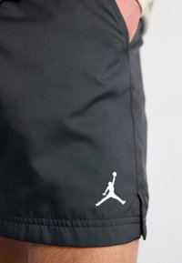 Black sports shorts made from smooth fabric featuring a white Jumpman logo on the lower left side; includes side slit design.