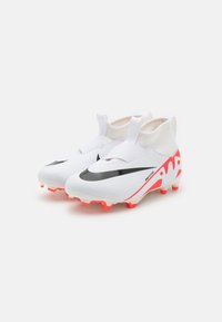 Scarpette da calcio bianche sportive con logo Nike nero, dettagli rossi sulla suola, design elastico simile a una calza e tomaia testurizzata per una migliore presa.