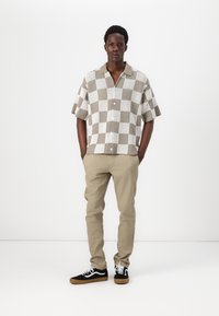 Kortärmad skjorta med knappslå i ett rutigt mönster i beige och vitt. I kombination med beiga byxor och svarta sneakers med vita accenter.