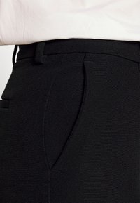 Svarta skräddarsydda byxor med en slät, texturerad tyg, veckad front och sidofickor, designade med en åtsittande midja.