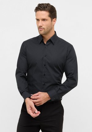 Schwarzes Langarmhemd mit einem weißen Punkte-Muster, Button-Down-Kragen und taillierter Passform, kombiniert mit schwarzen Hosen.