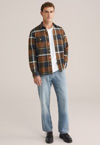 Rjava in modra karirana srajca, z gumbi, z dvema žepoma na prsih, kombinirana z svetlo modrimi jeans hlačami in črnimi čevlji. Gladka tekstura, sproščen kroj.