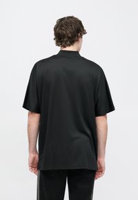 Čierna polokošeľa s krátkym rukávom vyrobená z hladkej látky, má golier a voľný strih. Minimalistický dizajn bez viditeľných vzorov alebo ozdôb.