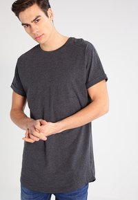 Camiseta de manga corta en gris oscuro, hecha de material suave, con cuello redondo y puños enrollados, y un dobladillo en la parte posterior ligeramente más largo.
