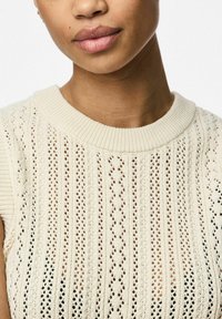 Stickad tröja i cream med ribbat rundhals; har ett strukturerat mönster av vertikala ränder och öppet arbete genom hela plagget.