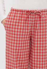 Rode en witte geruite pyjamabroek met een elastische tailleband en verstelbaar trekkoord, voorzien van zijzakken en een zachte, geweven textuur.