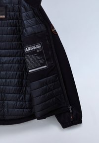 Giacca nera imbottita con rivestimento interno trapuntato, tasche con zip e etichette con marchio; tessuto esterno opaco con polsini elastici.