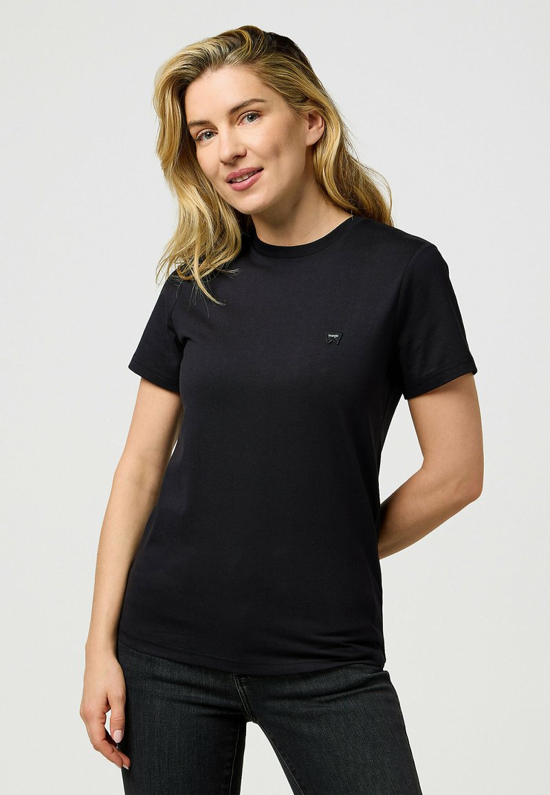 Sort bomulds t-shirt med korte ærmer, rund halsudskæring og et lille emblem på venstre bryst. Glat tekstur, tætsiddende pasform.