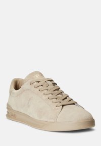 Beige mockask sneakers med rund tå, texturerad yta och kontrasterande snörning. Har en subtil logotyp och en vadderad sula.