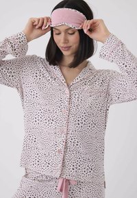 Ljusrosa leopardmönstrad pyjamasuppsättning med en knappar-up topp som har en bröstficka och matchande byxor, kompletterad av en ljusrosa ögonmask med broderi.
