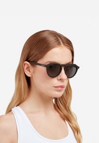 Mustad mustad prillid tumedate läätsedega, minimalistliku disainiga ja matt viimistlusega. Raam on kerge ja siledate servadega.