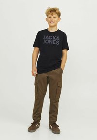 T-shirt preto de manga curta com "JACK & JONES" em texto cinza escuro, combinado com calças cargo castanhas com bolsos laterais e um corte relaxado.