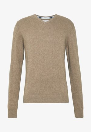 V-kaklo megztinis, pagamintas iš minkšto, šviesiai rudo mezginio audinio, su ilgomis rankovėmis ir gulinčiais rankovių bei apykaklės kraštais. Audinyje subtili tekstūra.